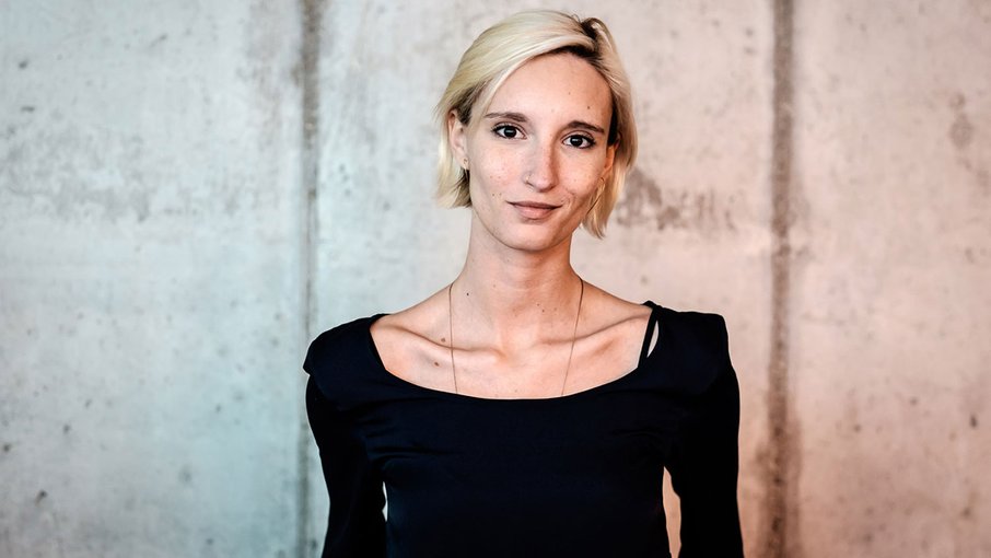 Denise Linke Eine junge Frau mit blonden Haaren steht vor einer Betonwand.
