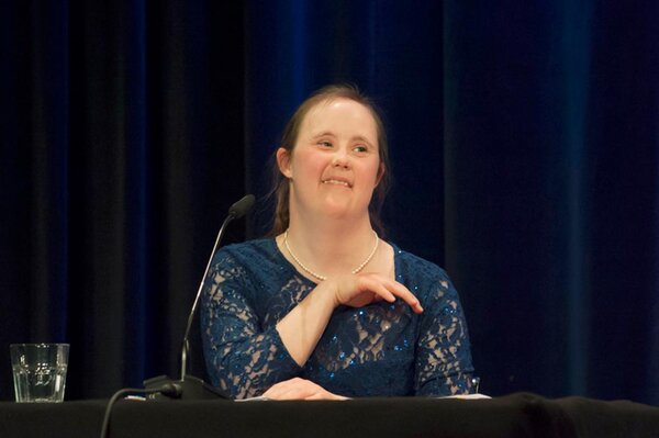 Eine junge Frau mit Sown-Syndrom auf der Bühne an einem Lesetisch, sie lacht