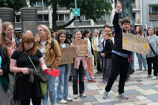 Jugendliche demonstrieren auf einem Platz für Inklusion und bessere Unterstützung. Ihre Schilder fordern unter anderem: „Therapie ist wichtig!“ und „Inklusion – sonst knallt’s“.