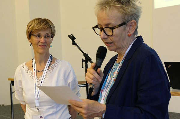 Man sieht links die Referatsleiterin Christine Reichel aus dem NRW-Ministerium für Arbeit, Gesundheit und Soziales und rechts die Moderatorin, die sie vorstellt.