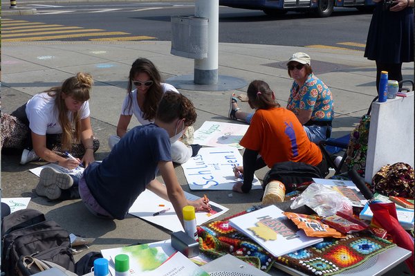 Fünf Personen sitzen auf dem Boden und malen Plakate. 