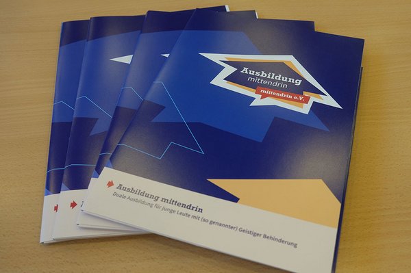 Auf einem Tisch liegen aufgefächert die Informationsmappen zum Fachtag. Auf der Mappe erscheint das Logo Ausbildung mittendrin