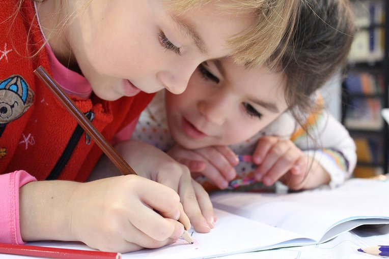 Schüler:innen Nahaufnahme zweier Kinder, die über ein Heft gebeugt sind. Eines von ihnen schreibt etwas in das Heft.