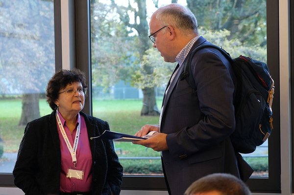 Eine Frau steht links im Bild und ein Mann rechts im Bild, die Beiden sind in einem Gespräch vertieft