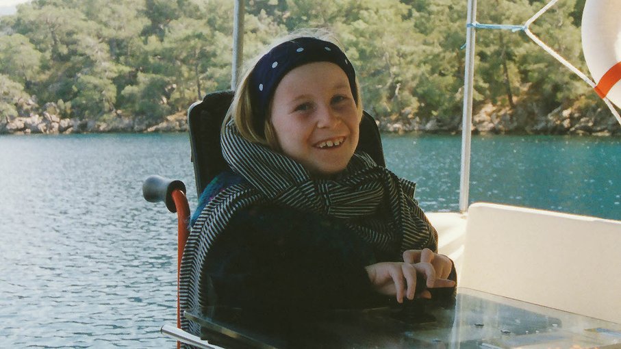 Anne Ein Foto der jungen Anne Gersdorff. Sie lächelt breit, trägt ein schwarzes Haarband mit weißen Punkten und einen gestreiften Schal