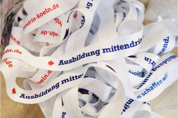Auf dem Foto sieht man ein Knäuel weißer Lanyards mit dem Schriftzug „Ausbildung mittendrin“ „mittendrin e.V.“ und „Inklusion schaffen wir!“ in blau und rot.