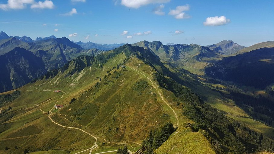 Kleinwalsertal Eine grüne Berglandschaft, oben im Bild blauer Himmel mit einigen weißen Wolken.