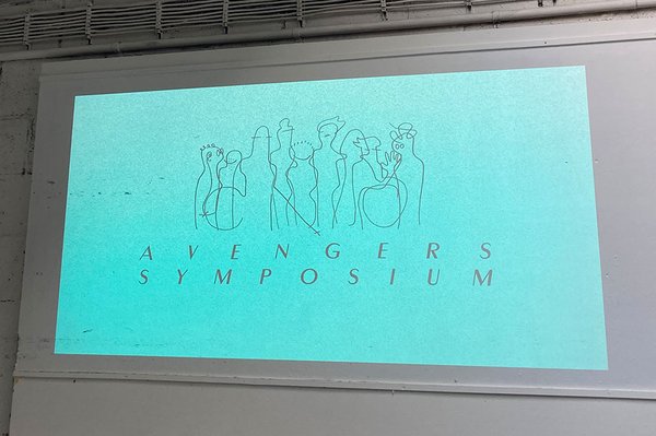 Wand mit Projektion: Türkiser Hintergrund mit Text: AVENGERS-Symposium