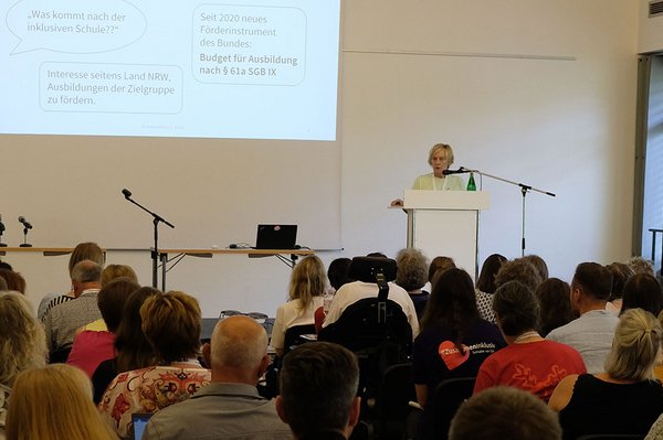 Eva-Maria Thoms steht am Rednerpult und spricht zu einem gut gefüllten Saal.