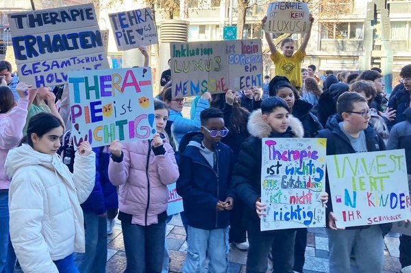 Schülerinnen und Schüler demonstrieren auf einer Straße und halten selbstgemalte Schilder hoch, auf denen unter anderem „Therapie ist wichtig“ und „Inklusion ist kein Luxus“ steht.