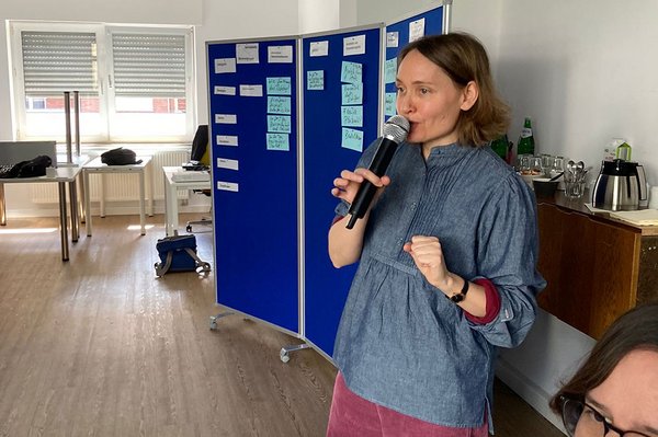 Tina Sander mit Mikro in Workshop-Raum, im Hintergrund eine Stellwand mit aufgepinnten Karten