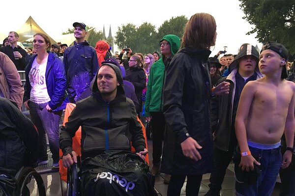 Zuschauer mit und ohne Behinderung bei Open-Air-Konzert, ein junger Mann mit freiem Oberkörper, die anderen mit Regenjacken.
