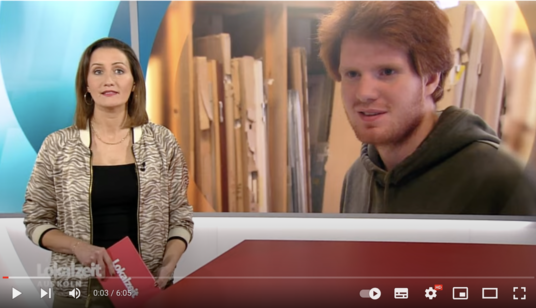 WDR Lokalzeit Screenshot des Youtube-Videos: Links im Bild die Moderatorin, dahinter eingebkendet Dominik, ein junger Mann mit roten Haaren, er steht vor einem Regal mit Holz und lächelt.