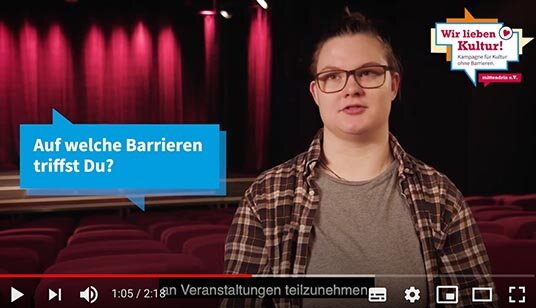 Screenshot von einem Youtube-Film. Eine Frau mit kurzen Haaren und Brille schaut in die Kamera. Neben ihr steht eine Sprechblase mit dem Text „Auf welche Barrieren triffst du?“