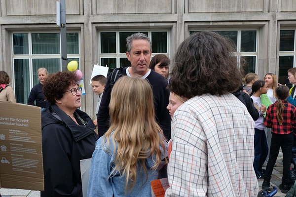 Erwachsene und Jugendliche stehen während der Demonstration in kleinen Gruppen zusammen und diskutieren. Im Hintergrund sind weitere Teilnehmende und bunte Luftballons zu sehen.