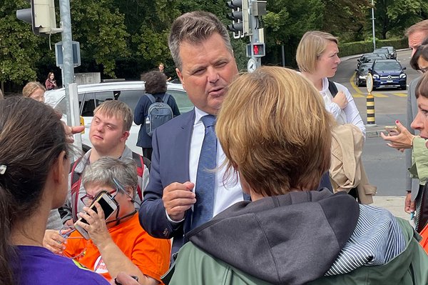 Zwei Personen sprechen miteinander, weitere Personen stehen drumherum.