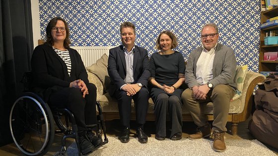 Gruppenfoto auf Sofa vor gemusterter Tapete, von links nach rechts: Monika Wolter im Rollstuhl, daneben auf dem Sofa Jürgen Dusel, Tina Sander und Andreas Huckschlag