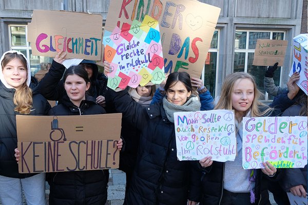 Jugendliche halten Schilder vor sich mit der Aufschrift: Rollstuhl = keine Schule?