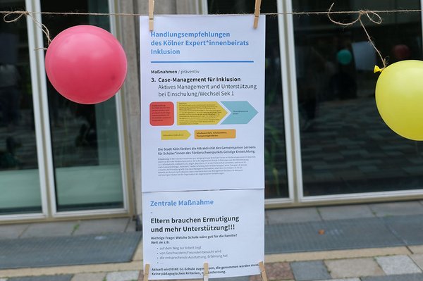 Zwischen einem roten und einem gelben Luftballon hängen Informationen des Kölner Expert*innenbeirats Inklusion. Sie fordern besseres Fallmanagement sowie mehr Ermutigung und Unterstützung für Eltern.