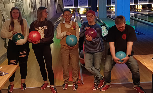 Fünf junge Auszubildende stehen vor einer Bowling-Bahn und haben jeder eine Bowling-Kugel in der Hand