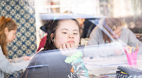 Jugendliche mit Downsyndrom schaut nachdenklich aus einem Fenster.